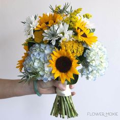 a person holding a bouquet of sunflowers and hydrangeas in their hand