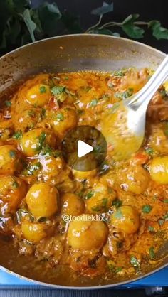 a pan filled with potatoes and sauce on top of a stove next to a wooden spoon