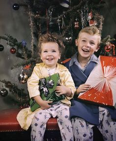 two young boys sitting on a bench in front of a christmas tree holding gifts and smiling