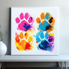 an art print of colorful hand prints on a white wall next to a vase and plant