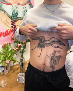 a man with a bird tattoo on his stomach is standing in front of a painting