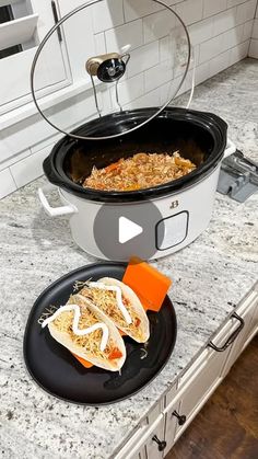 two black plates with food in them sitting on a counter top next to a slow cooker