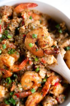 a white bowl filled with shrimp and rice next to a wooden spoon on top of a table