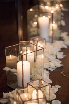 some candles are sitting in glass containers on the ground with flowers and petals around them