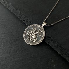 Saint George was a Christian who is accepted as a saint in Christianity. According to traditional rumors, he was a soldier in the Roman army. This silver coin necklace tells the story of St.George and the dragon. Diameter 25 mm Story The tradition tells that a fierce dragon was causing panic at the city of Silene at the time George arrived there. In order to prevent the dragon from devastating people from the city, they gave two sheep each day to the dragon, but when the sheep were not enough they were forced to sacrifice humans instead of the two sheep. The human to be sacrificed was elected by the city's own people and one time the king's daughter was chosen to be sacrificed but no one was willing to take her place. George saved the girl by slaying the dragon with a lance. The king was s Mythological Engraved Round Pendant Jewelry, Mythological Silver Jewelry With Coin Pendant, Silver Mythological Jewelry With Coin Pendant, Mythological Silver Round Pendant Necklace, Silver Mythological Round Pendant Necklace, Symbolic Coin Pendant Necklace For Commemoration, Symbolic Silver Medallion Necklace With Coin Pendant, Collectible Spiritual Coin Necklaces, Commemorative Silver Coin Necklace