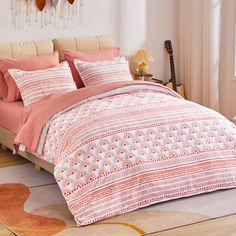 a bed with pink and white comforters in a room next to a wall mounted clock