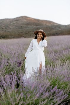 a woman in a white dress and hat walking through lavender fields