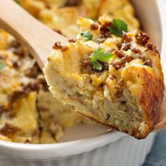 a close up of a casserole in a white dish with a wooden spoon