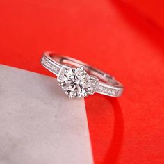 a diamond ring sitting on top of a piece of white paper next to a red background