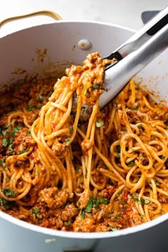 spaghetti being cooked in a pot with a ladle full of sauce and parsley