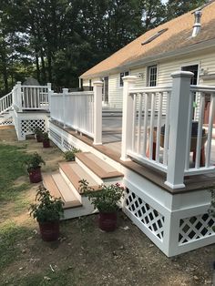 a white deck with steps and planters on the grass next to it in front of a house