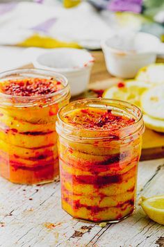 two jars filled with food sitting on top of a wooden table next to lemons