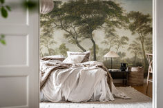 a bedroom scene with focus on the bed and wallpaper that has a tree painted on it