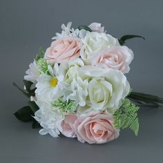 a bouquet of white and pink flowers on a gray background with greenery in the foreground