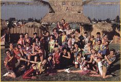 a group of people posing for a photo in front of a tiki hut with thatched roof