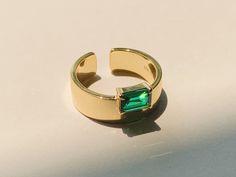 Embrace the timeless allure of the Emerald Monolith Ring, our latest addition to the collection. This exceptional piece showcases an exquisite baguette-cut emerald, beautifully nested in a 14K gold-plated open cigar band. Its bold monolithic style, enriched by the natural elegance of the emerald, makes this ring an unmissable statement piece. Infuse your everyday look with the vibrant charm of this ring. Lab-grown emerald stone size: 5mm x 7mm; Band width: 7mm. Band is made of 14k Gold plated st Modern Gold Emerald Open Ring, Modern Gold Emerald Baguette Cut Ring, Modern Gold Emerald Cut Ring, Gold Emerald Ring With Rectangular Stone, Minimalist Emerald Cut Gold Emerald Ring, Minimalist Gold Emerald Cut Emerald Ring, Gold Emerald Open Ring, Gold Open Ring With Emerald, Gold Rectangular Emerald Ring For May Birthstone