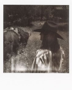 a black and white photo of a woman in a hat looking at an animal behind her