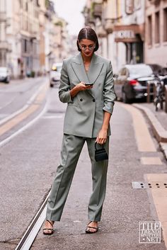 a woman is standing on the side walk looking at her cell phone and holding a purse