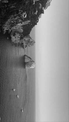 black and white photograph of people walking on beach next to cliff with ocean in background