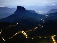 an aerial view of a mountain with lights on the road and mountains in the background