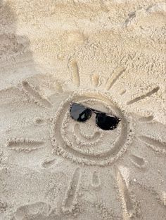 a smiley face drawn in the sand with sunglasses