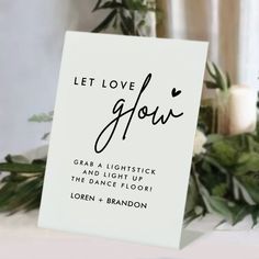 a sign that says let love grow on it next to some greenery and candles