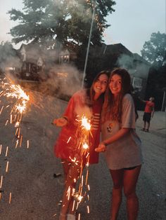 two girls standing next to each other holding sparklers