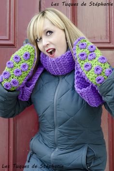 the woman is holding her mitts up to her ears while wearing a purple and green crocheted scarf