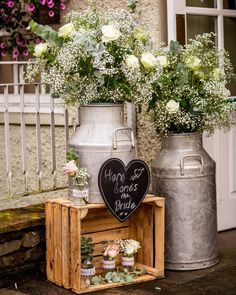 two metal vases with flowers in them sitting on a wooden crate next to each other