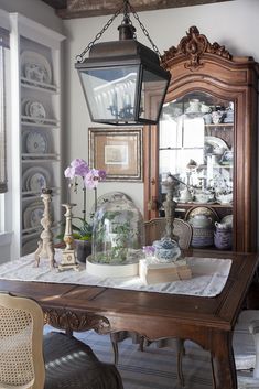 a dining room table with an old fashioned light hanging from the ceiling and some vases on it