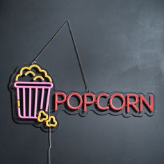 a neon sign that says popcorn hanging from a hook on the wall next to a black wall