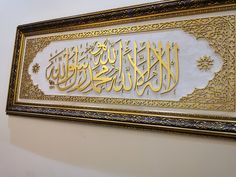 an arabic calligraphy displayed on the wall in a room with white walls and gold trimmings