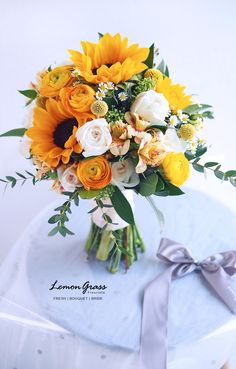 a bouquet of sunflowers and roses sits on a white table with a gray ribbon