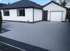 a white house with black roof and two garages on the side of the road