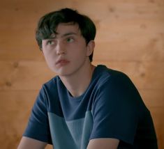 a young man sitting in front of a wooden wall