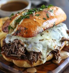 a sandwich with meat, cheese and sauce on a wooden platter next to french fries