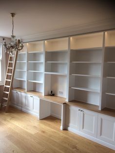 an empty room with white bookcases and ladder