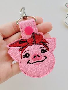 a hand holding a pink pig keychain with a red bow on it's head