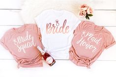 three bridesmaid shirts and a bottle of wine on a white wooden floor with flowers