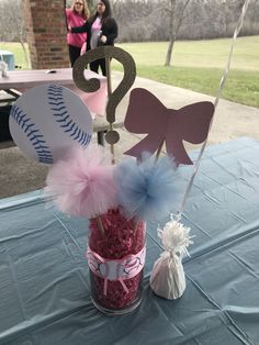 a baseball themed centerpiece sits in a vase on a blue table cloth with pink and white pom poms