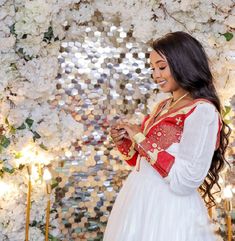 a woman standing in front of a floral wall using her cell phone while wearing a red and white dress