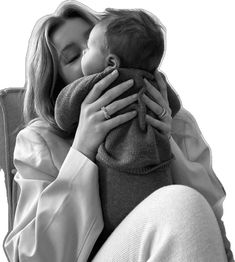 a woman sitting in a chair holding a baby and kissing her face with both hands