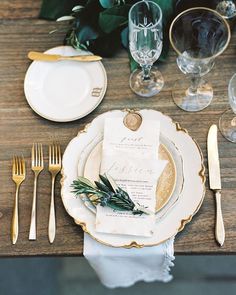 a place setting with gold and white plates, silverware, napkins and greenery