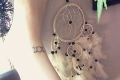 a woman's arm with a tattoo on it and a white dream catcher hanging from the wall