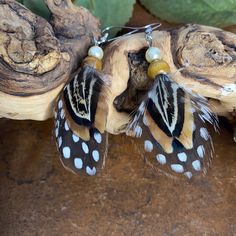 two brown and white butterflies with pearls hanging from them's earwires on a piece of wood