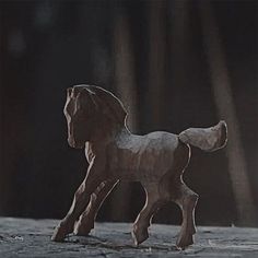 a wooden toy horse standing on top of a stone floor in front of a dark background