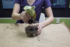 a woman is sitting at a table and holding a potted plant with dirt in it