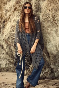 a woman standing in front of a rock wearing sunglasses and a knitted cardigan