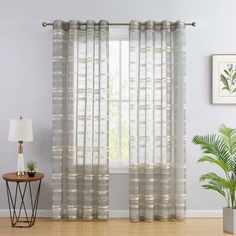 a living room with white walls and wooden flooring, two windows covered in sheer curtains