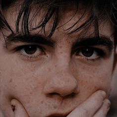 a young man with freckled hair is holding his hands to his face and looking at the camera